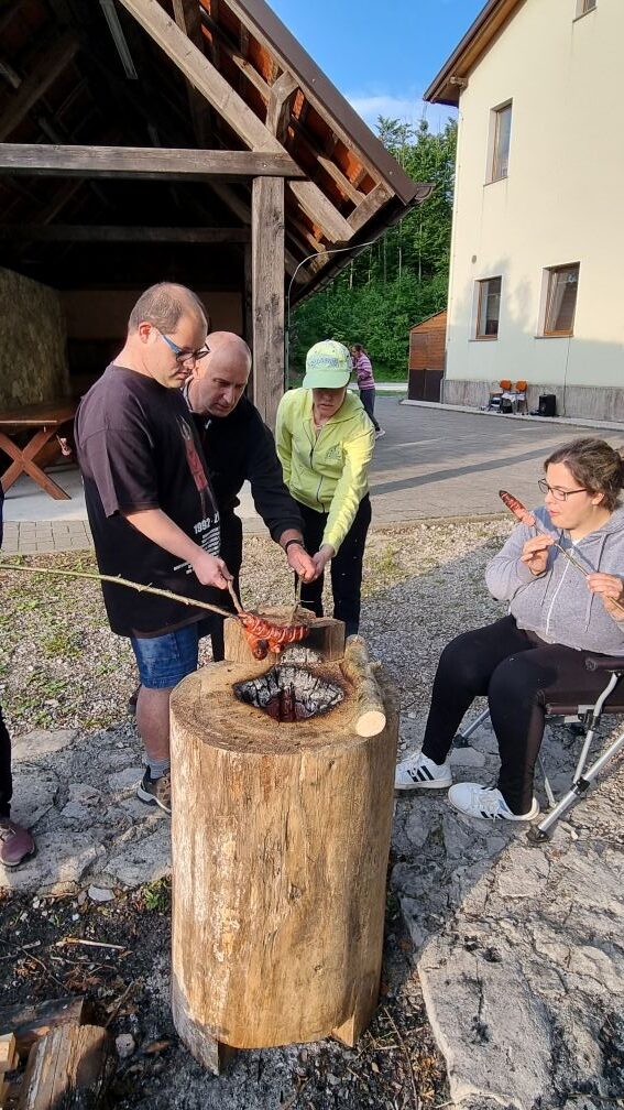 Uporabniki si pečejo klobase, ki so jih prej napičili na dolge leskove palice.
