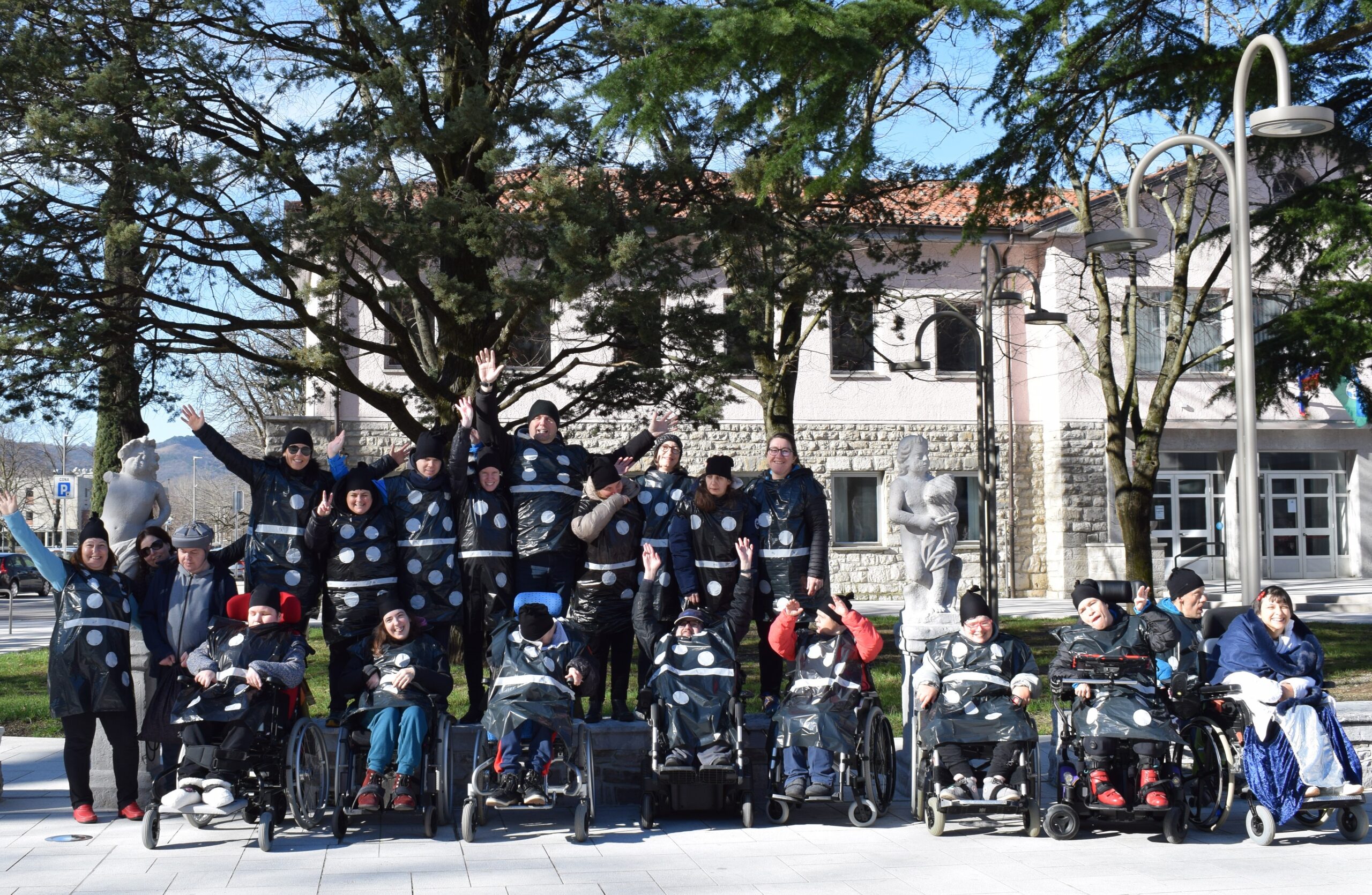Putne maske na trgu v Vipavi. Na sliki je skupina iz enote vipava oblečena v kostume, ki predstavljajo domine. Bele pike na črnih kostumih.