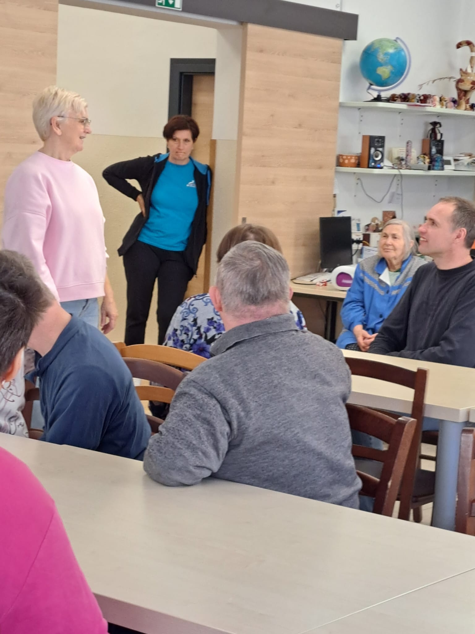 Na sliki je gospa damjana, ki vodi delavnico in nekaj udeležencev. So v večnamenskem prostoru.